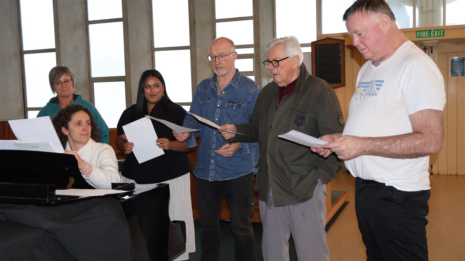 Adult choir rehearsing around the piano